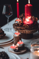 Rustic table decor for Christmas or New Year family dinner. Centrepiece with red candle, dry orange, cone, cinnamon, anise. Zero waste eco-friendly home. Cozy atmosphere, dark background. Close up