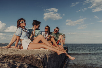 Fototapeta premium Group of happy young friends enjoying beer while spending carefree time seaside together