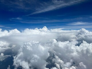 Wide aerial, cumulus clouds below, cirrus clouds with deep blue sky above, seen through aircraft window