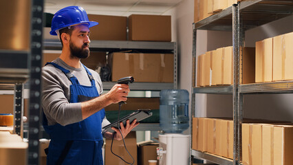 Male supervisor scanning barcodes on packages in depot, pointing scanner at cardboard boxes and checking stock. Man in overalls holding tablet in storage room, industrial merchandise.