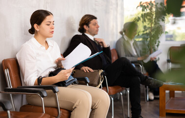 Fototapeta premium Young businesswoman preparing to negotiations with investors, reading documents while waiting for meeting in office lobby
