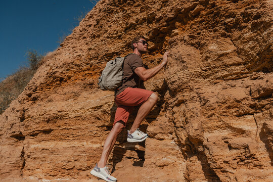 Courageous male adventurer with backpack holding on grip while climbing the rock