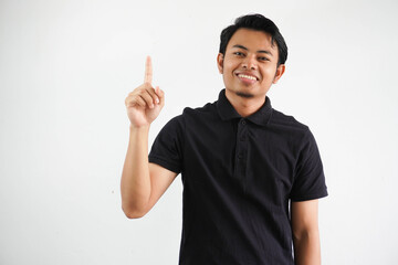 smiling young asian man pointing up with happy face expression wearing black polo t shirt isolated on white background