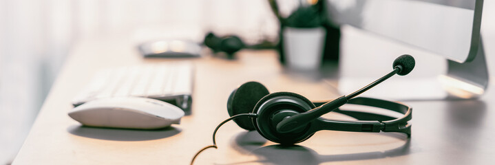 Panorama view of empty call center operator workspace, focused on headset. Representing corporate...