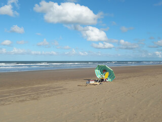 Fototapeta na wymiar Peaceful vacation beach scene. A parasol on the sand, endless horizon, sunny sky, calm sea.