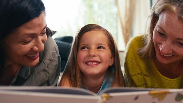 Close up of same sex family with two mature mums and daughter lying on floor reading a book together - shot in slow motion