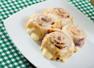 Appetizing rolled cinnamon buns in sugar and vanilla icing on white plate..