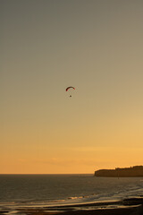 Paraglider flying on a beach cliff at sunrise