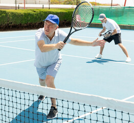 Portrait of concentrated elderly man playing tennis with friend on court.