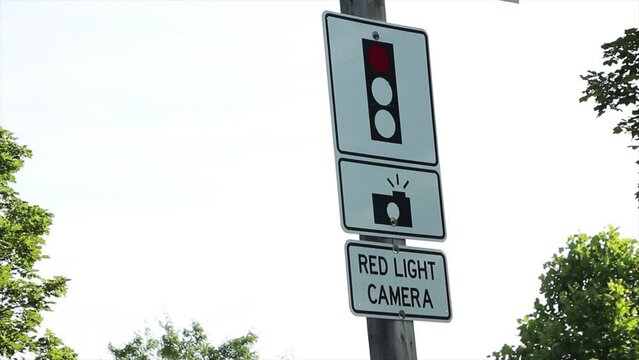 red light camera sign with picture of camera flashing and red traffic light on white background, followed by drive away