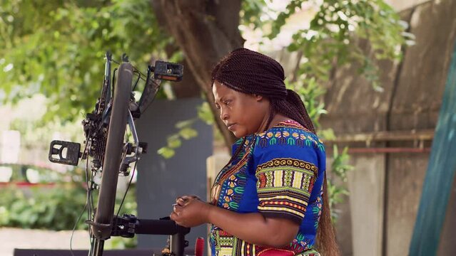 Determined female cyclist using specialized work tool to repair and adjust bike rear derailleur. Sporty african american woman mending her bicycle with professional multitool in home yard.
