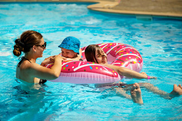Children with mom have fun in the pool on a hot summer day.