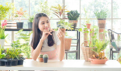 Obraz na płótnie Canvas Portrait garden beautiful pretty young Asian girl woman wearing white blouse with long black hair and smile fresh with bright smile look pot small tree leaf green plant in room shop Happy and relax