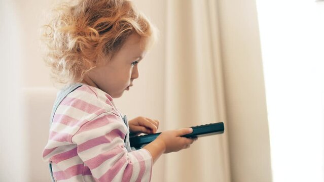 Little girl watches TV and uses a TV remote to switch channels