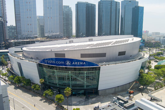 Crypto.com Arena with skyscrapers, hotels and office buildings in the city skyline, lush green trees, cars, and people on a summer day in Los Angeles California USA