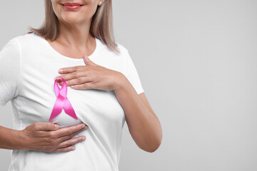 Woman with pink ribbon on light grey background, closeup and space for text. Breast cancer awareness