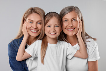 Three generations. Happy grandmother, her daughter and granddaughter on light gray background