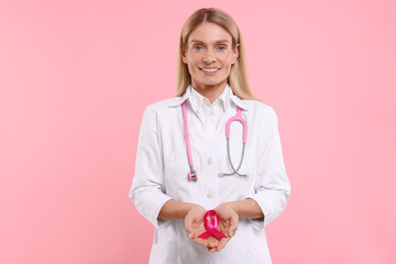Doctor with stethoscope holding pink ribbon on color background. Breast cancer awareness