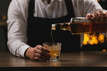 Bartender pouring whiskey from bottle into glass at bar counter indoors, closeup