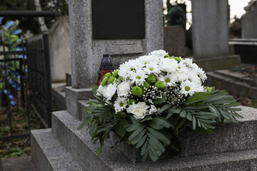 Fototapeta na wymiar Funeral wreath of flowers on granite tombstone in cemetery