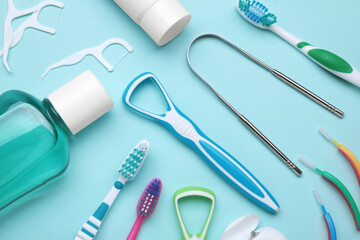 Tongue cleaners and other oral care products on light blue background, flat lay