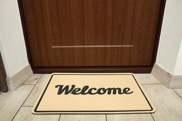 Beautiful beige doormat with word Welcome on floor near entrance