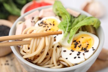 Eating delicious ramen from bowl with chopsticks, closeup. Noodle soup