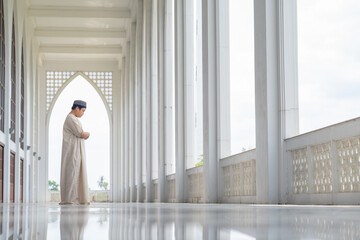 A little Asian Muslim boy is praying with peace in the beautiful mosque, giving a powerful atmosphere of faith, with copy space, islam concept.