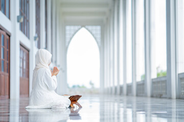 The image of an Asian Muslim woman in the Islamic religion in hijab in cream color. reading the Quran and having a happy Staying in a beautiful mosque, Arabic word translation: The Holy Al Quran.