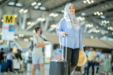 An Asian Muslim wearing a blue hijab is preparing for a vacation and she is at the international airport. She is waiting for her friends, Muslim travelers.