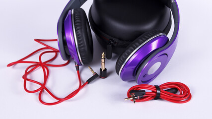 Purple headphones with cables and connectors and case lays on light background.