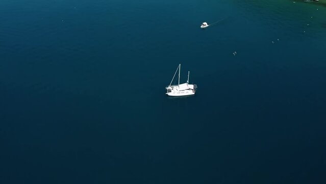 Aerial view of white catamaran anchored in blue waters with small tourist motor boat passing by