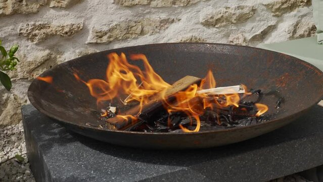 Fire burning in a round cast iron fire pit in front of a stone wall, close up shot. 