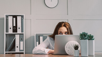 Hiding freelancer. Laptop work. Lazy woman scared of boss pretending busy using computer looking with frightened eyes sitting at office workplace.