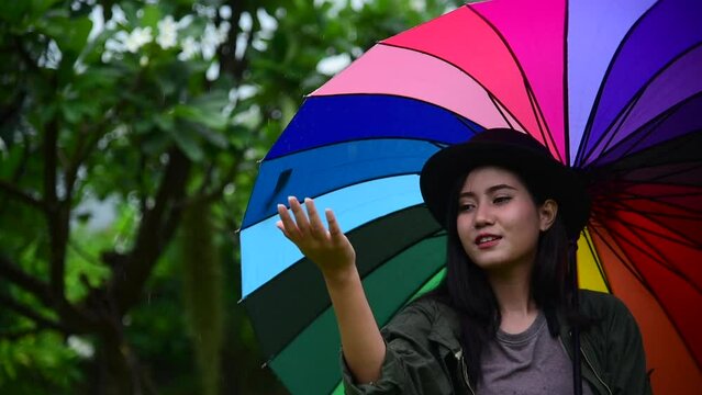Young woman holding multicolor rainbow umbrella outdoor. Asian women hold rainbow umbrella outdoor in green nature park. LGBTQ gay pride concept
