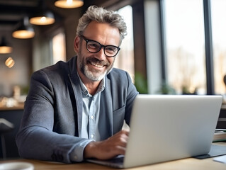 Fototapeta premium Happy Businessman using laptop computer in office. Older casual man working online on terrace of cafe