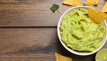 Bowl of delicious guacamole, lime and nachos chips on wooden table, top view. Space for text
