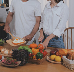 Handsome man sitting near his wife at kitchen. Family couple see social media, surf the web while sitting at kitchen table with generic laptop. Couple working with laptop at home