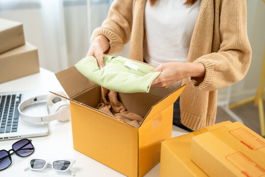 Woman business owner at fashion store packing clothing in the parcel cardboard box and delivery to customer. Asian female entrepreneur working in clothes shop.