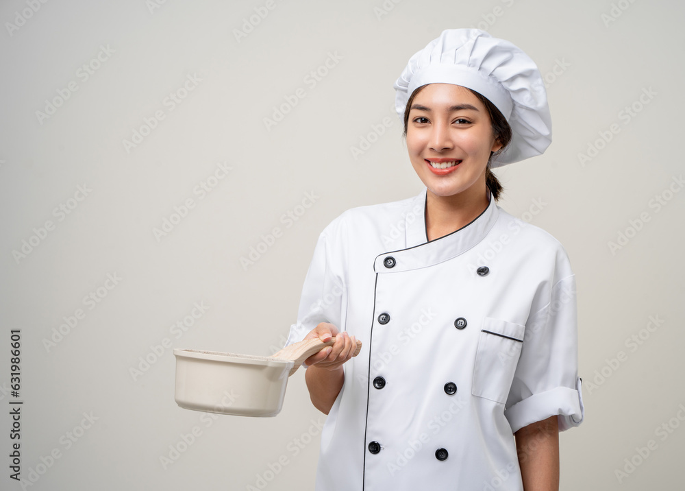 Wall mural young beautiful asian woman chef in uniform holding soup pot ladle utensils cooking in the kitchen v