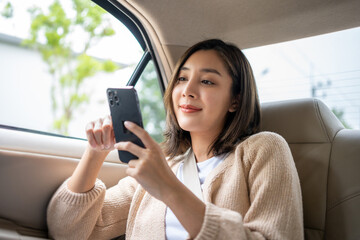 Relaxing moment of beautiful woman sitting in car back seats using smartphone play social media...