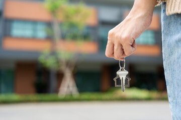 Woman buying or rent new home she holding key front of new house. Surprise happy young asian woman giving house key and smile to rent or purchase apartment home. Moving relocation concept.
