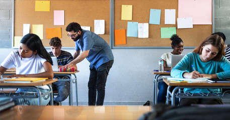 Male teacher helps teen male high school student with lesson in the background. Classmates focused on the task at hand. - obrazy, fototapety, plakaty
