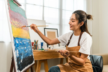 Asian woman artist working on painting with brush and variant acrylic color. Female artist painter...
