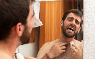 young man in pain grooming shaving and trim the beard with electric razor cutting mustache on the...