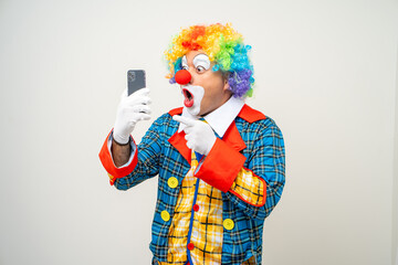 Mr Clown. Portrait of Funny face Clown man in colorful uniform standing holding smartphone. Happy expression male bozo in various pose with cellphone on isolated background. - obrazy, fototapety, plakaty