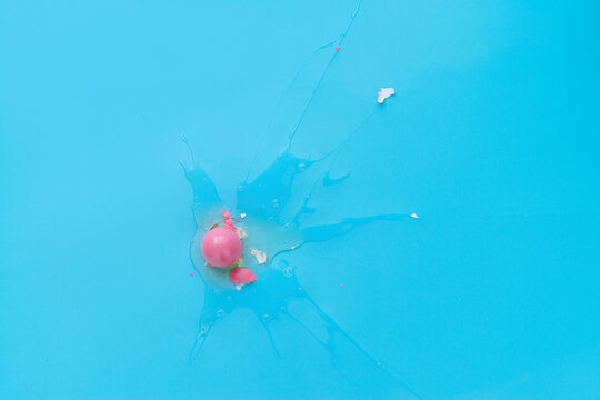 Top view of broken raw egg covered with bright pink paint against turquoise background 