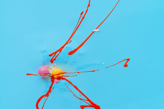 Cracked raw egg lying on blue table surface, red oil paint partly covered its yolk and bright pink shell