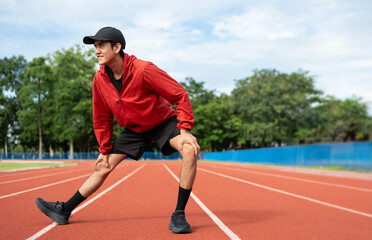 Obraz premium Young asian man wearing sportswear running outdoor. Portraits of Indian man stretching leg before running on the running track at sport stadium. Training athlete work out at outdoor concept.