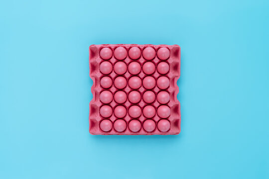 Directly above view of bright pink egg tray with thirty eggs prepared for Easter celebration against turquoise background 
